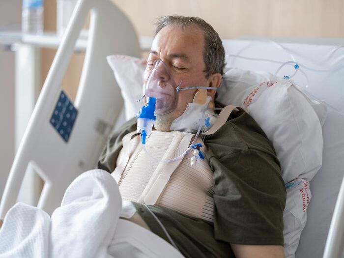 An elderly patient lies in a hospital bed with an oxygen mask and medical devices, depicting a disturbing scene.