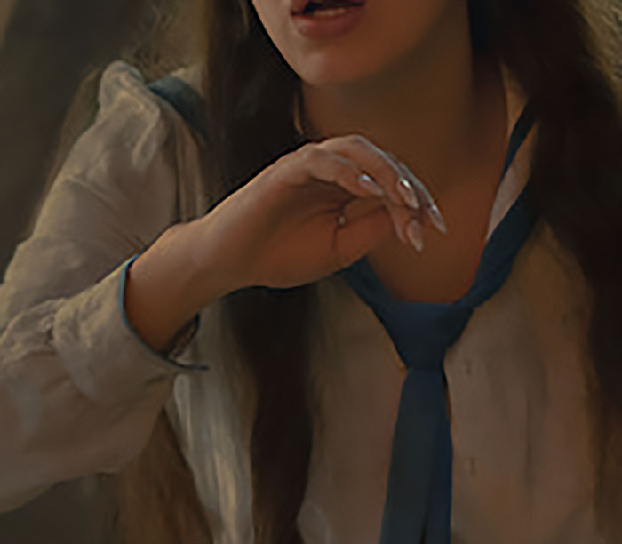 Close-up of a female with long nails, wearing a shirt with a blue tie, possibly Millie Bobby Brown for Enola Holmes 3.