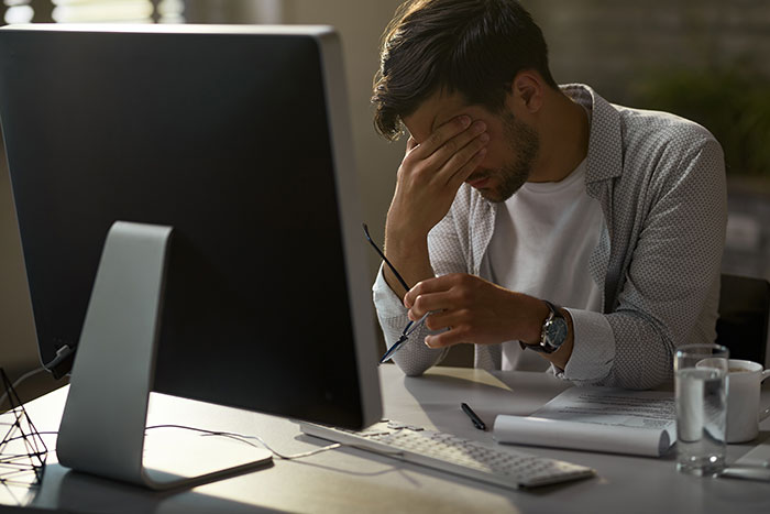Stressed woman holding glasses, sitting at desk with computer, worried about long commute after work from home canceled. Stressed woman holding glasses, sitting at desk with computer, worried about long commute after work from home canceled.