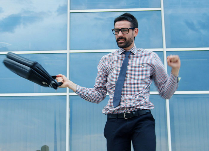 An excited employee in a plaid shirt and tie, holding a briefcase, celebrating revenge against a horrible boss.