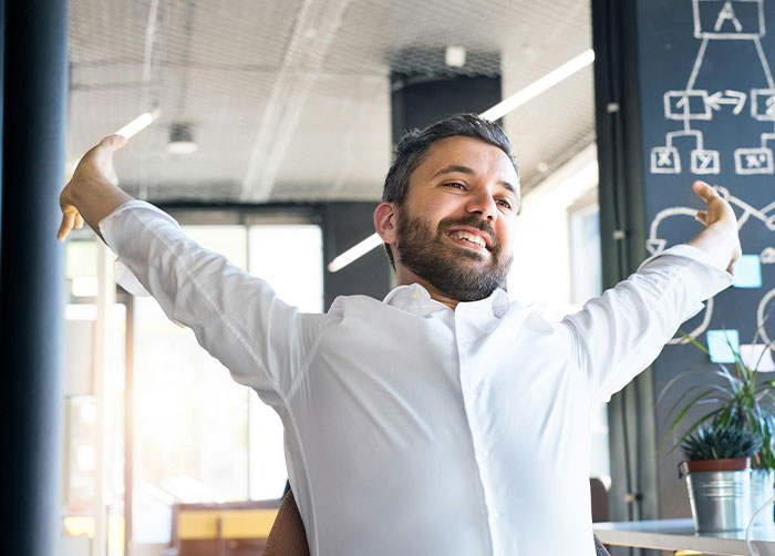 A smiling man in a white shirt stretches his arms wide, feeling the perfect revenge on a horrible boss.