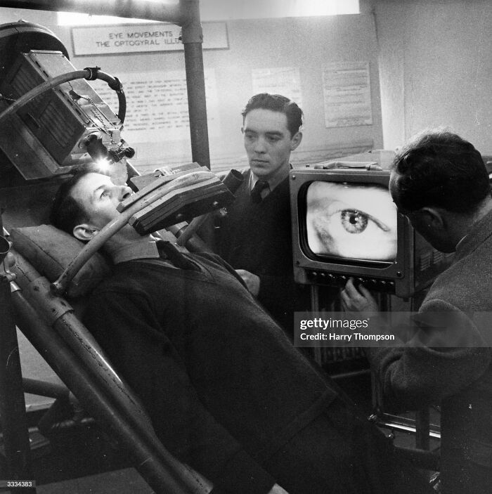 Vintage medical devices in use showing early eye examination technology with patient and technicians in a clinical setting.