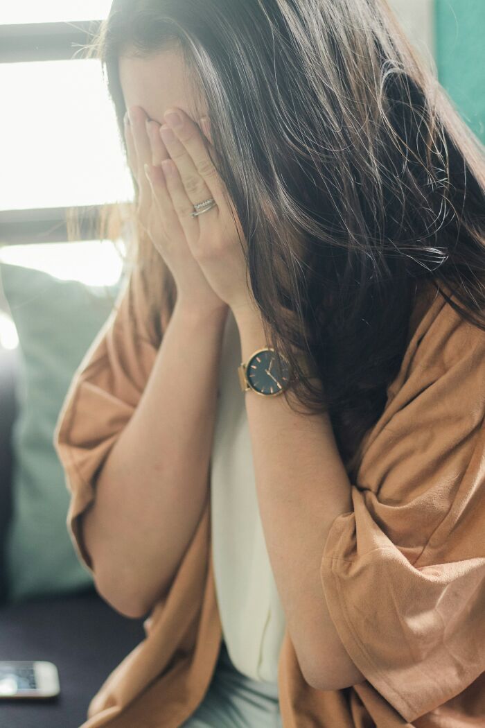 A woman hides her face in her hands, revealing a gold watch and ring, representing shared family secrets.