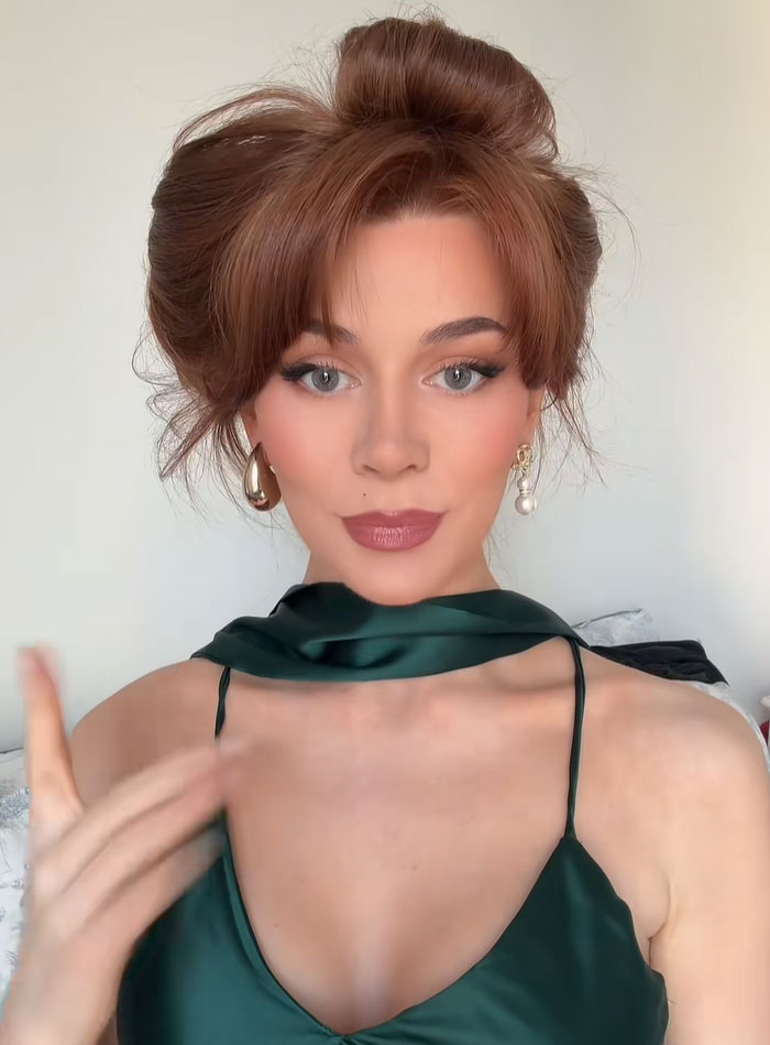 Young woman with reddish-brown hair in an updo, wearing a green silk dress and earrings, sparking a debate on society's new normal and facelift.