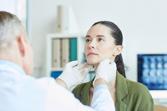 A doctor in white gloves examining a young woman's neck, sparking debate on societal beauty standards and facelift concerns.
