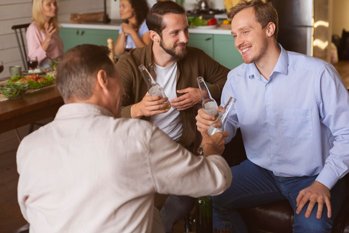 Three men enjoying drinks at a dinner party, one man acting like an expert while others listen and smile.