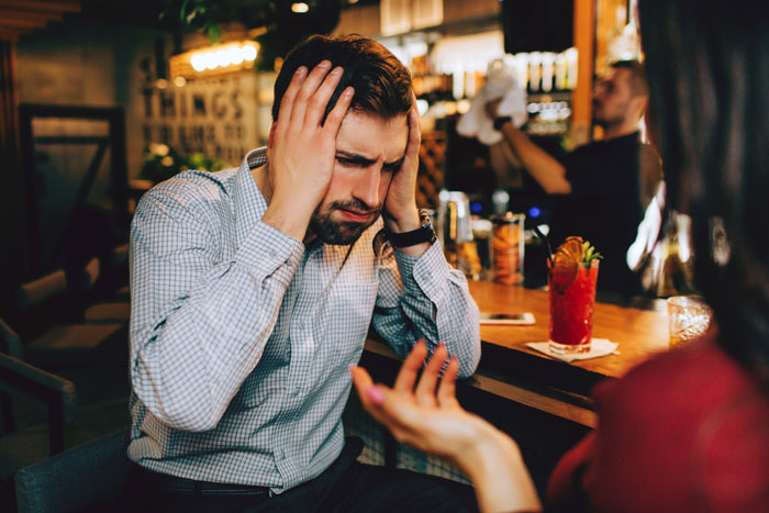 Man plays expert at dinner party looking frustrated while a woman questions him and challenges his knowledge.