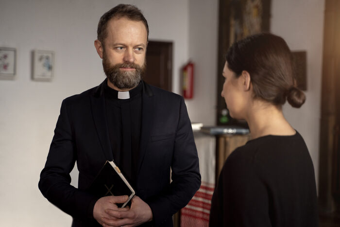 Man dressed as priest holding a book talking to woman, representing unexpected results from DNA tests discovery.