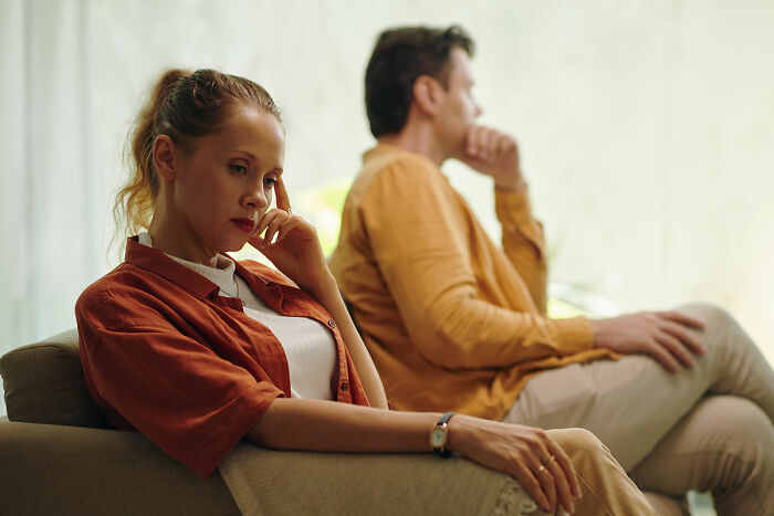 Couple sitting apart on couch looking thoughtful and distant after surprising DNA test results reveal unexpected heritage.
