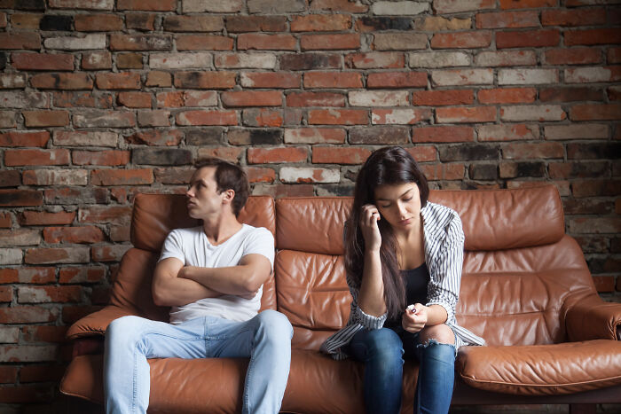 Young couple sitting apart on a couch looking upset, symbolizing unexpected DNA test results revealing heritage.