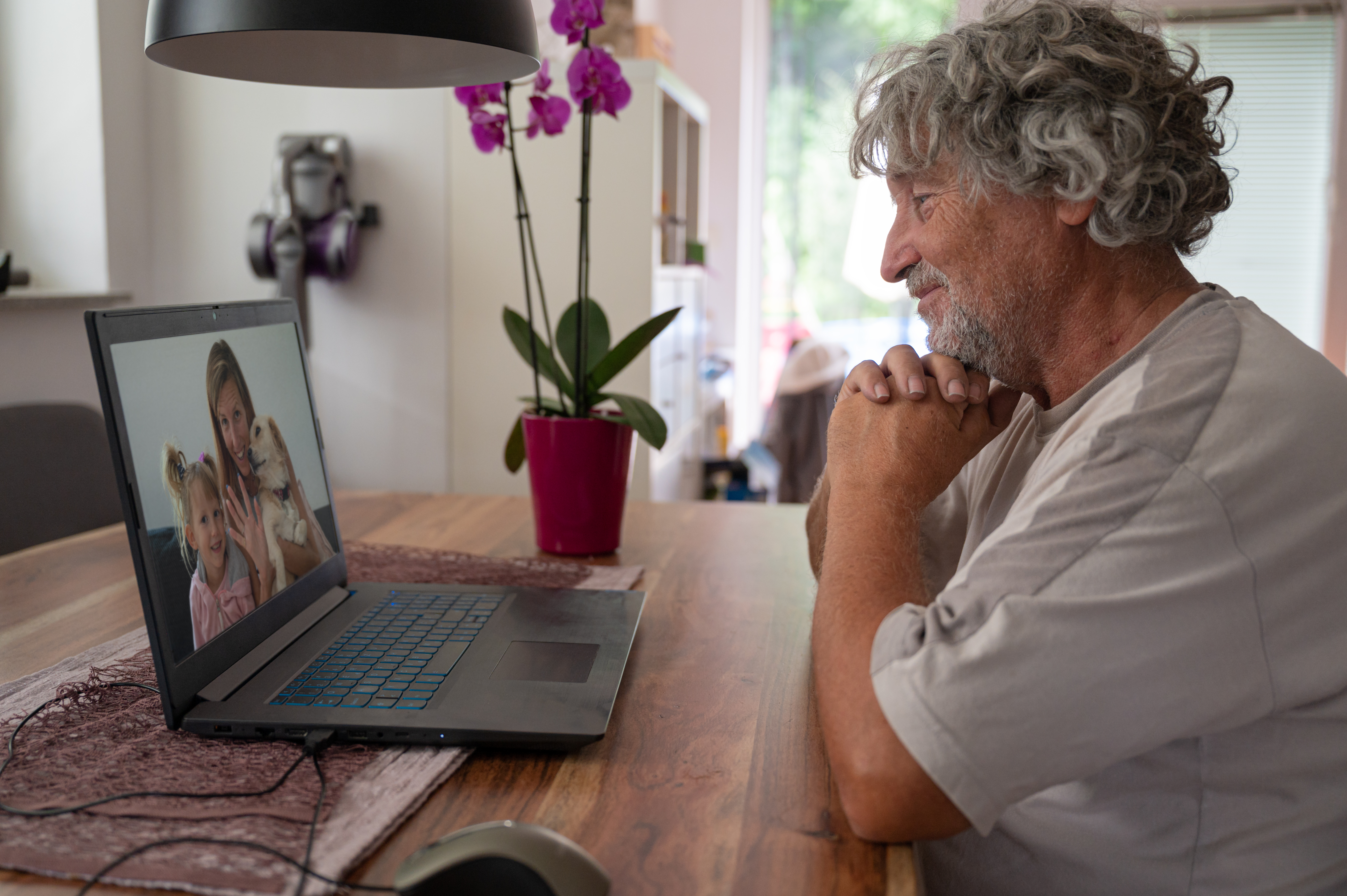 Older man video calling family, appearing thoughtful during conversation about controlling 20YO best friend concerns.