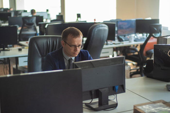 Man in glasses working at his computer in a busy office, highlighting the workplace environment for someone using a feeding tube.