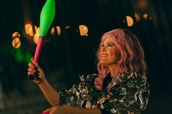 Person with pink hair and glitter makeup performing with colorful juggling clubs, illustrating unusual items TSA confiscates.