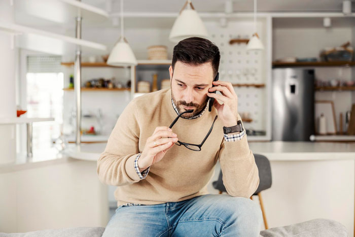 Man on phone, looking concerned, holding glasses. His hubs notices strange behavior on camera.
