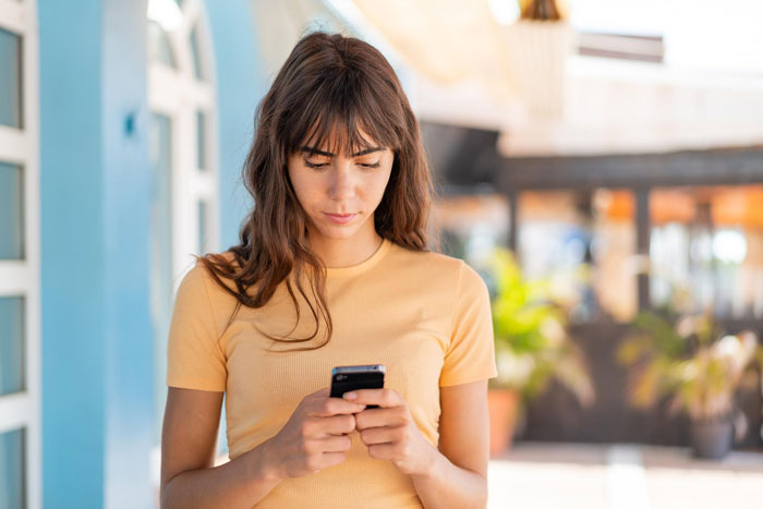 Woman in yellow shirt focused on her phone, reflecting feelings of testing friend to remind appreciation.