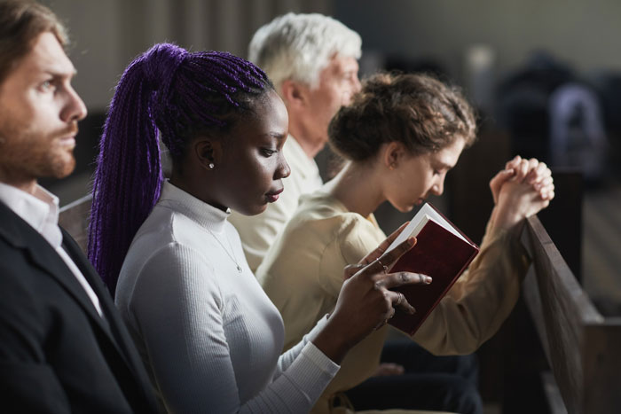 People in a church pew, some praying or reading a Christian Bible. This image evokes thoughts of a Christian bride.