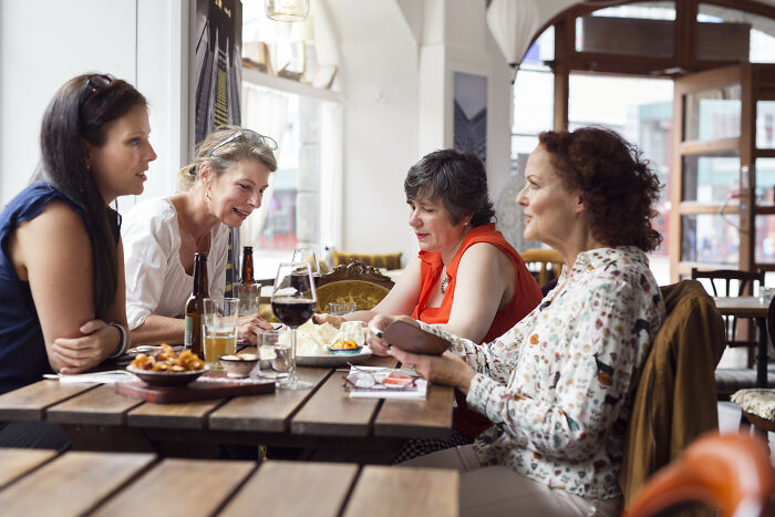 Four women sitting at a restaurant table enjoying food and drinks, capturing moments of satisfaction with staff service.