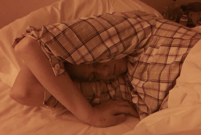 Person sleeping in a plaid shirt with arms wrapped around their head in a funny and unhinged sleeping position on a bed.