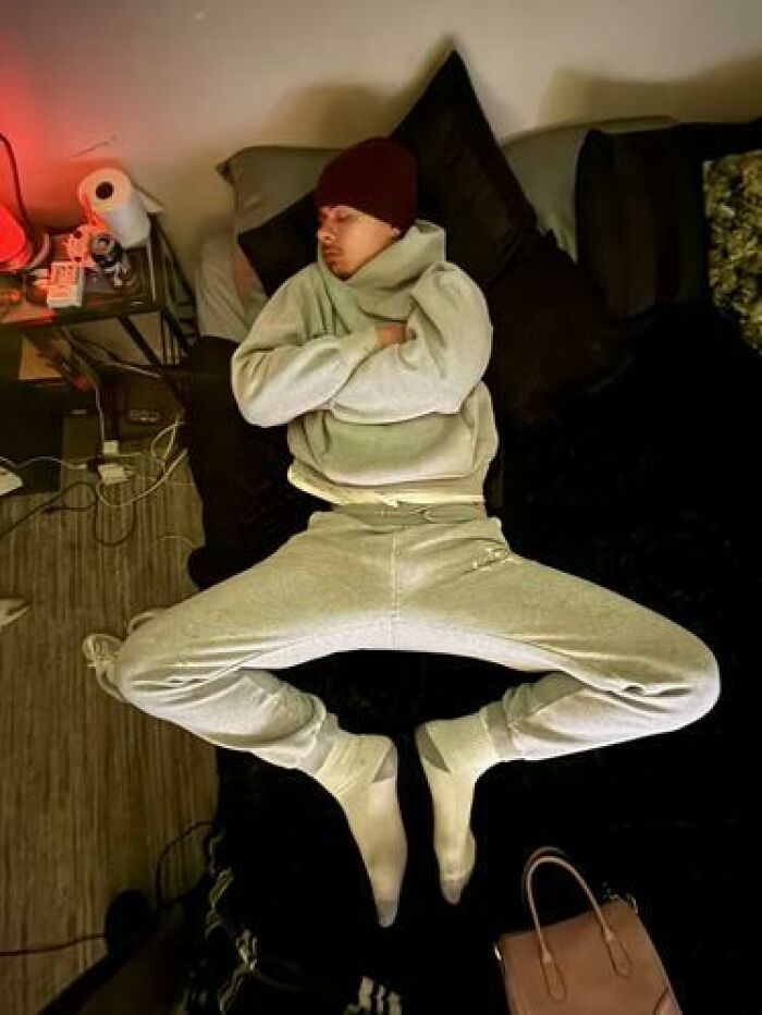 Person sleeping in hilarious and unhinged ways sprawled on a bed wearing casual clothes and a beanie hat.