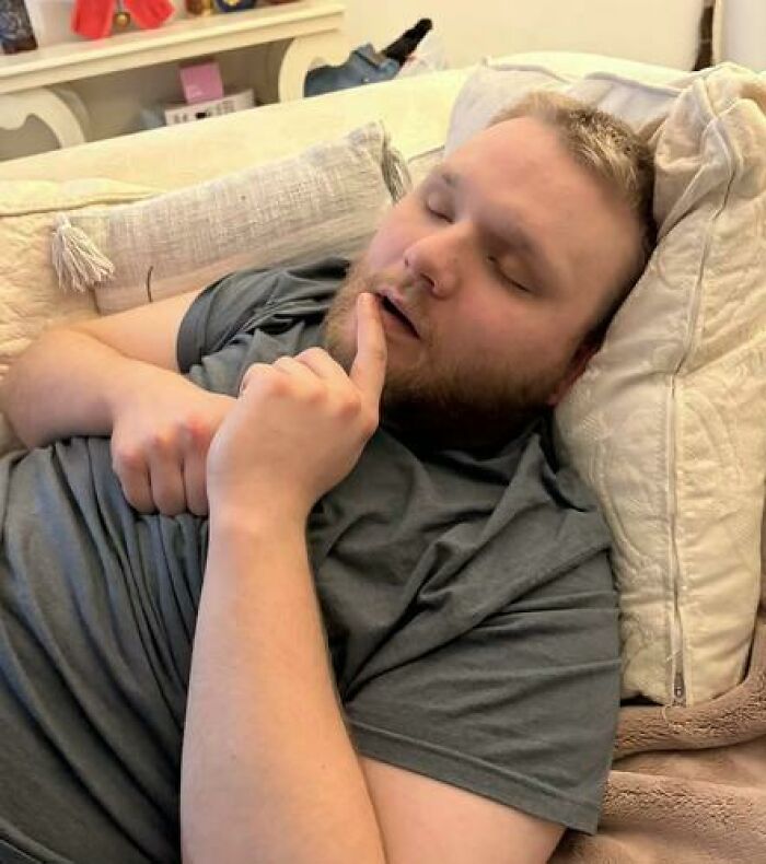Man caught sleeping in a hilarious and unhinged way on a couch with a finger resting near his mouth
