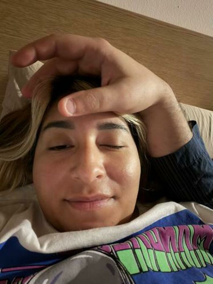 Person caught sleeping with a hand awkwardly placed on their forehead on a bed, showing a hilarious and unhinged sleep moment.