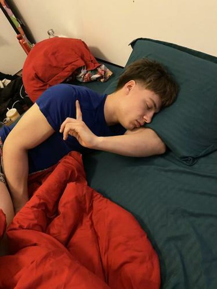 Young man caught sleeping in a funny position with arm bent under the head on a dark green pillow and red blanket nearby