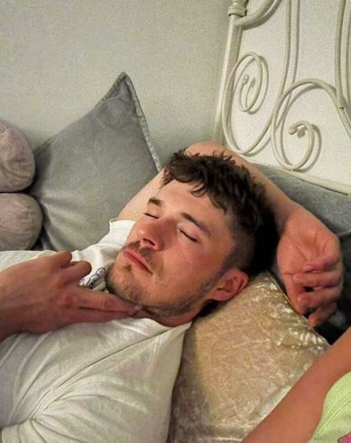 Man caught sleeping in hilarious and unhinged way with finger pointing at his chin while resting on a bed pillow.