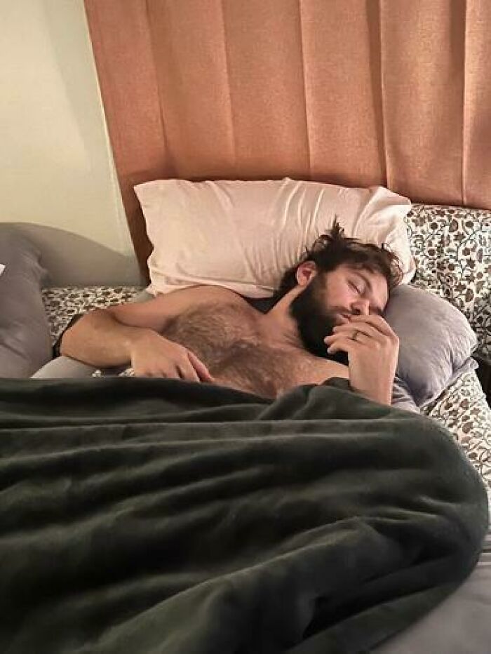 Man caught sleeping shirtless in bed with hand near face covered by a blanket in hilarious and unhinged ways.