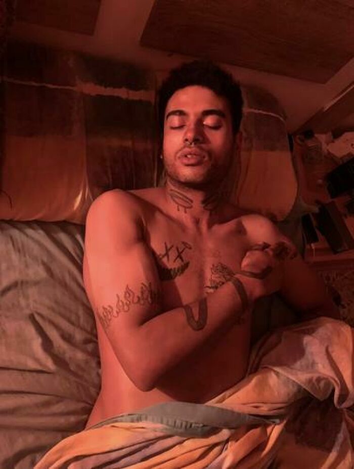 Young man with tattoos caught sleeping in an unusual and hilarious way under warm red lighting.
