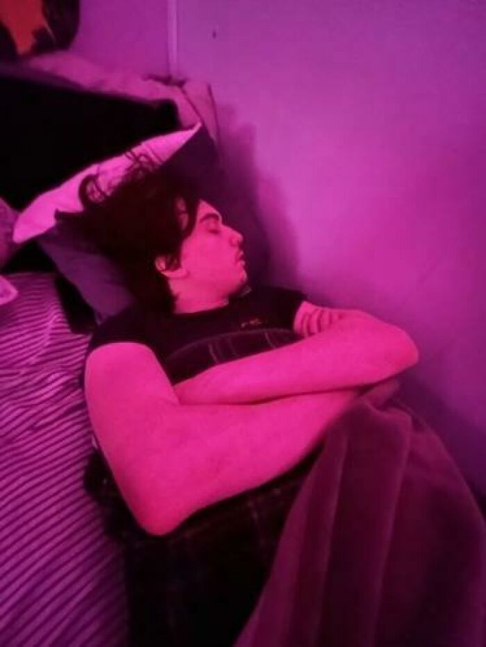 Person caught sleeping on a bed with arms crossed under vibrant pink lighting in a relaxed and unhinged manner.