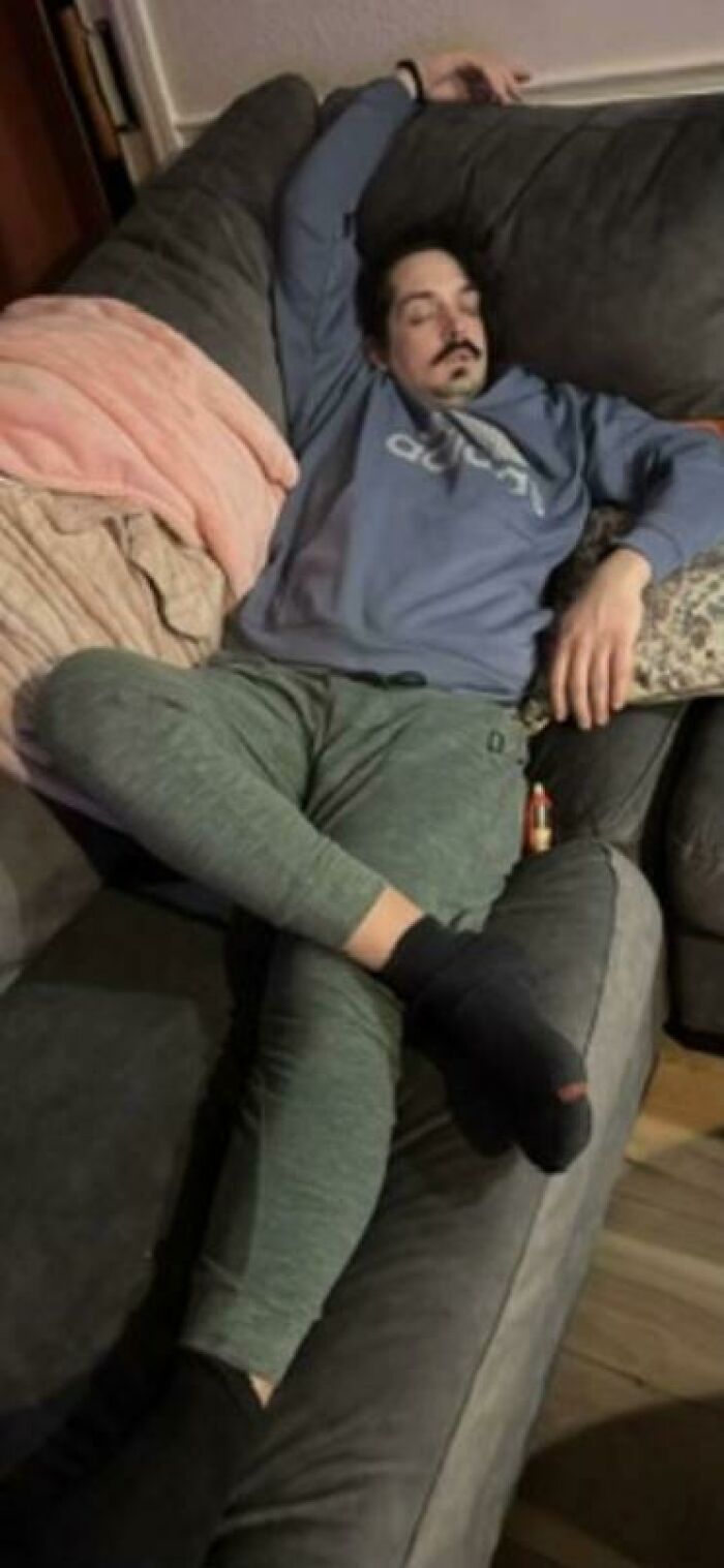 Man caught sleeping in hilarious and unhinged ways, sprawled awkwardly on a couch with one arm raised and leg crossed.