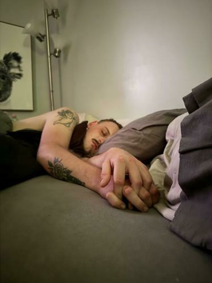 Man with tattoos sleeping in bed with hands clasped, caught sleeping in hilarious and unhinged ways.
