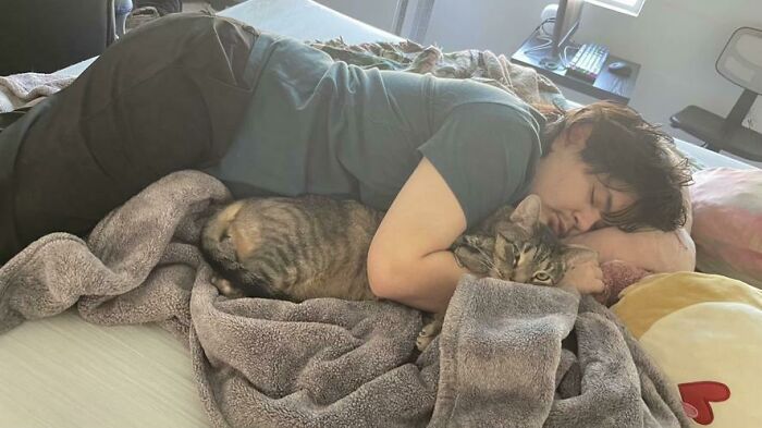 Person and cat caught sleeping in hilarious and unhinged ways, lying closely together on a cozy blanket.