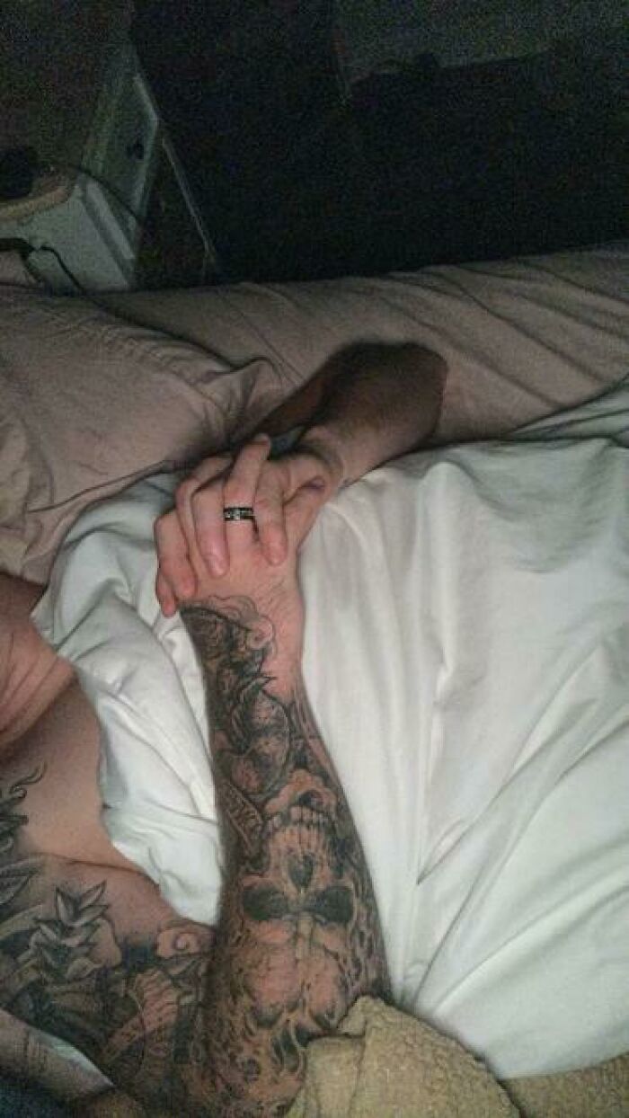 Tattooed person caught sleeping with hands clasped under white blanket in a dark room showing hilarious unhinged sleeping pose.