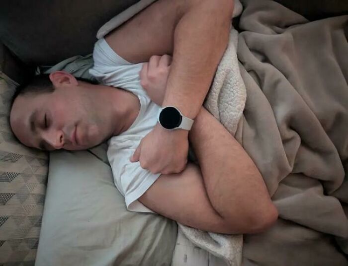 Man sleeping on bed wrapped in blanket with arms crossed, caught in a hilarious and unhinged sleeping position.