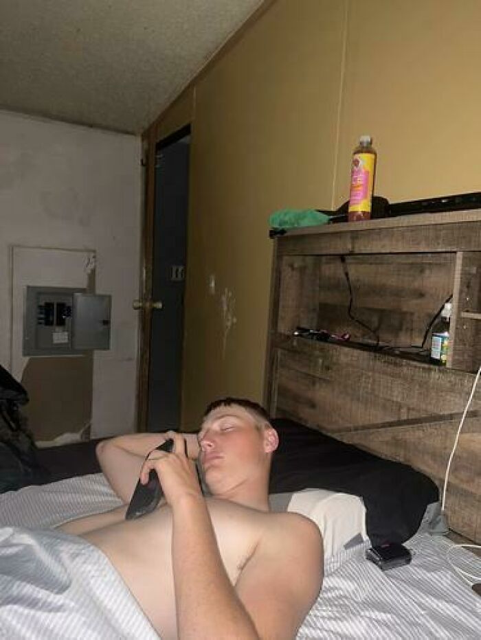 A man caught sleeping hilariously on a bed while holding a phone, showcasing unhinged sleeping positions.