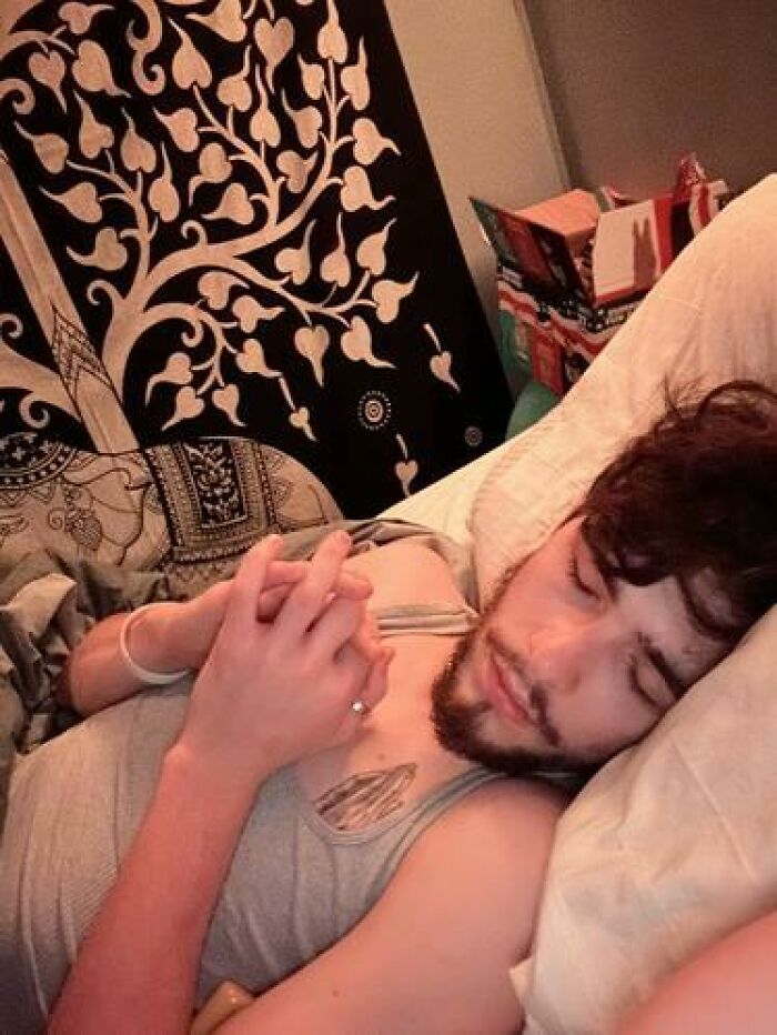 Person caught sleeping with hands clasped on chest, resting peacefully with a decorative tapestry in the background.