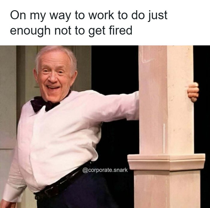 Older man leaning around a pillar with a smile, representing work memes about doing just enough to avoid getting fired.