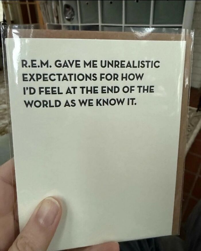 Hand holding a card with a relatable humor meme about unrealistic expectations and the end of the world.