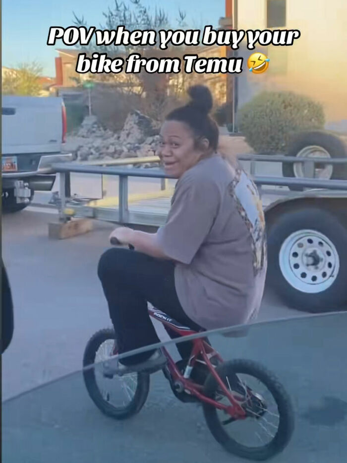 Woman laughing awkwardly riding a small bike bought from Temu outside with vehicles and trailer in the background.
