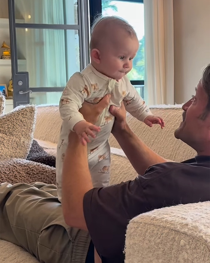 Gay dad playing with surrogate baby on couch, responding to backlash over video of baby crying for mama.