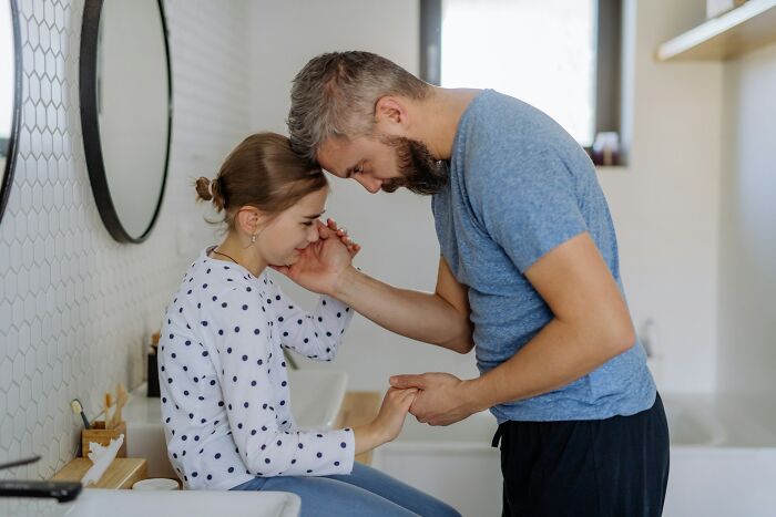 A dad comforts his daughter in a bathroom, holding her hand. Advice for dads raising daughters.