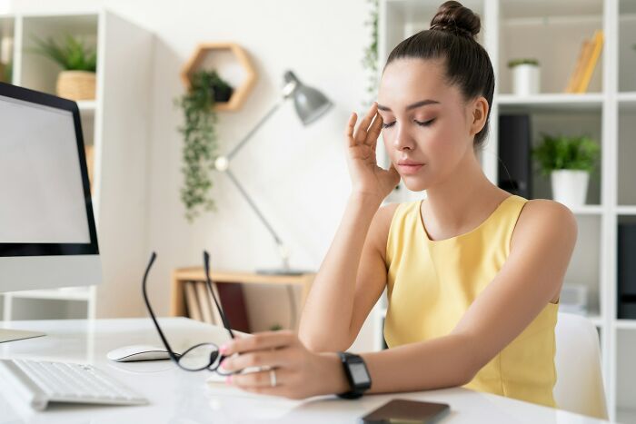 Young woman in yellow dress at office desk looking stressed after seeing an accidental message she sent out