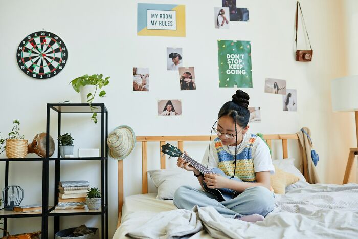 Young woman playing ukulele on her bed. A creative space that reflects a daughter's individuality for dads raising daughters.