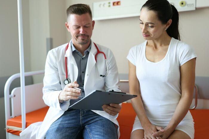 Gynecologist reviewing patient notes while a woman listens attentively during a medical appointment in a clinic room.
