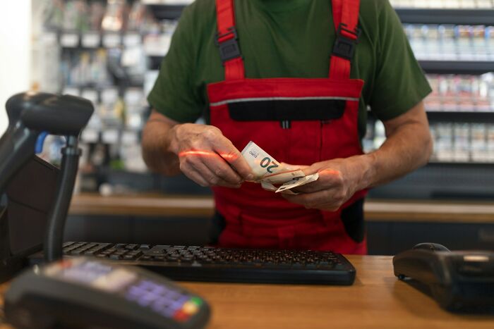 Man in red overalls counting cash behind a store counter representing encounters with former bullies in life.