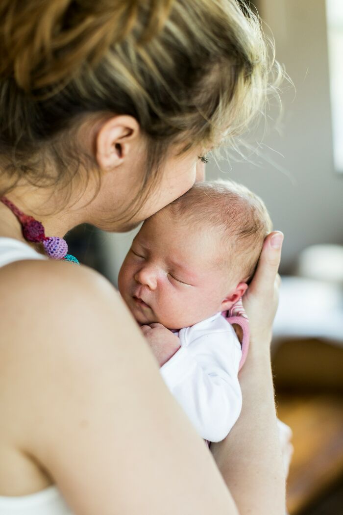 Mother gently holding and kissing her newborn baby, capturing a touching moment of love and care between moms and their children.