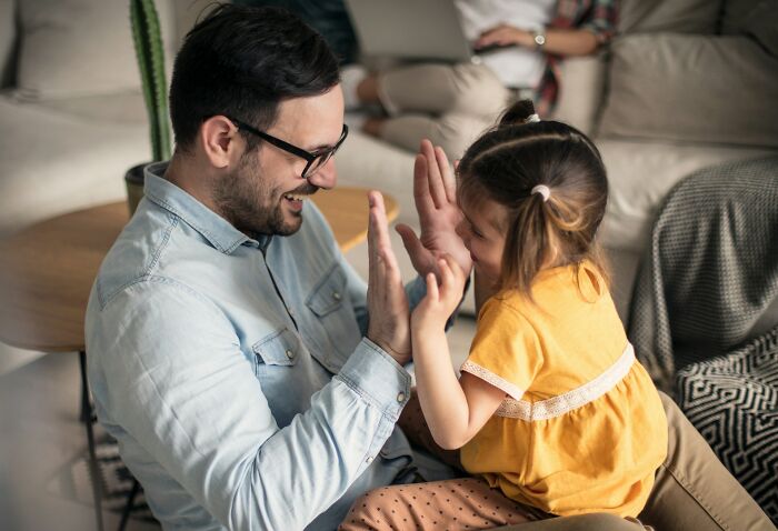 A smiling dad with glasses and a daughter playing patty-cake. Golden pieces of advice for dads raising daughters.