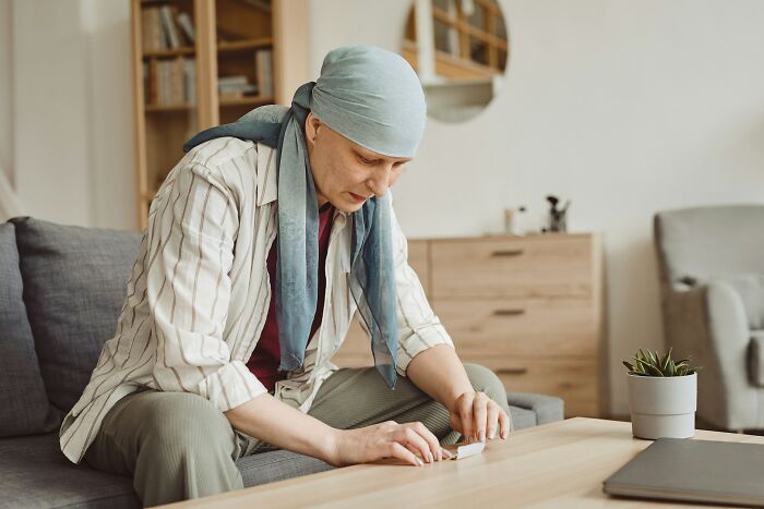 A person wearing a headscarf and striped shirt sits on a sofa, focused on something on the coffee table. God Bless America.