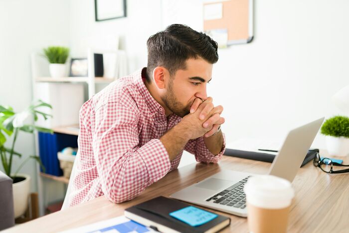 Man in red checkered shirt looking shocked at laptop screen after accidentally sending out a message, feeling mortified.